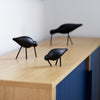 Black decorative birds on a wooden surface with a blue accent, featuring smooth, rounded shapes and minimalist design.