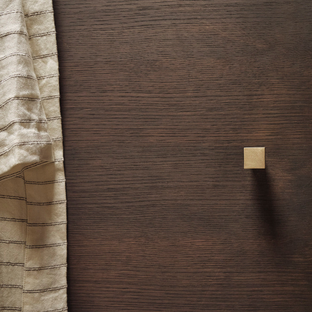 Elegant beige fabric with subtle stripes against a rich dark wood background, featuring a sleek gold square knob.