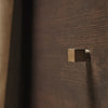 Brushed brass hook on a rich, dark wood background with subtle grain pattern. Elegant and modern design element.