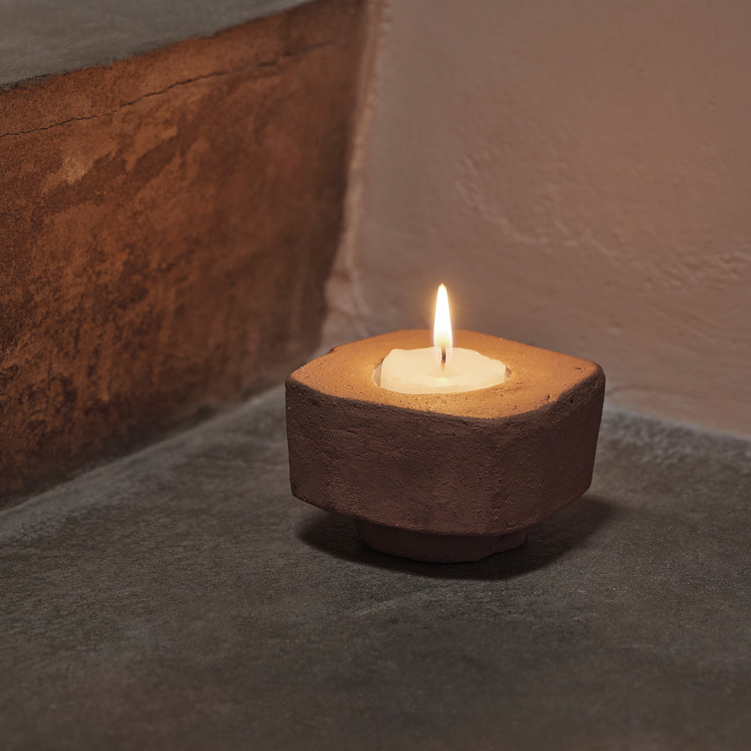 "Rustic brown candle holder with a natural texture and white candle, set on a muted gray surface."