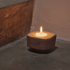 "Rustic brown candle holder with a natural texture and white candle, set on a muted gray surface."