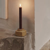 Dark burgundy candle with a textured, neutral-toned holder, set against a soft, light background.
