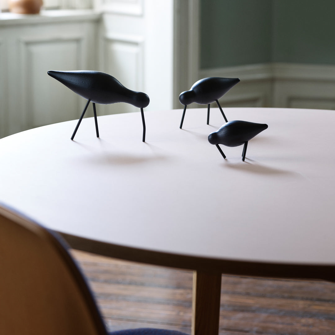 Black bird figurines on a light pink table surface, set against a neutral-toned backdrop. 