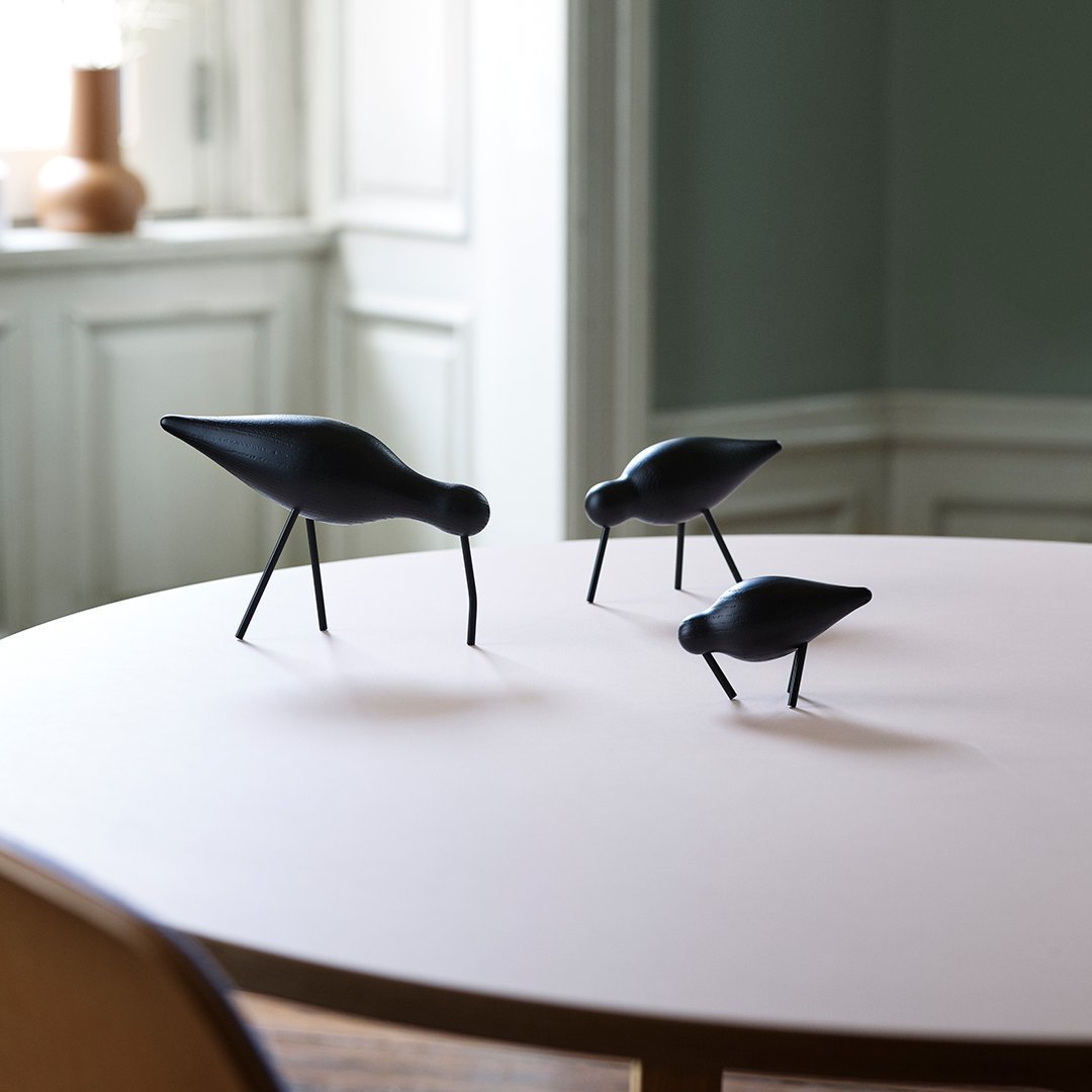 Three black bird sculptures on a round pink table, highlighting sleek shapes and minimalist design.