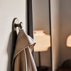Beige coat draped on a round metal hook against a neutral wall, with soft lighting in the background.