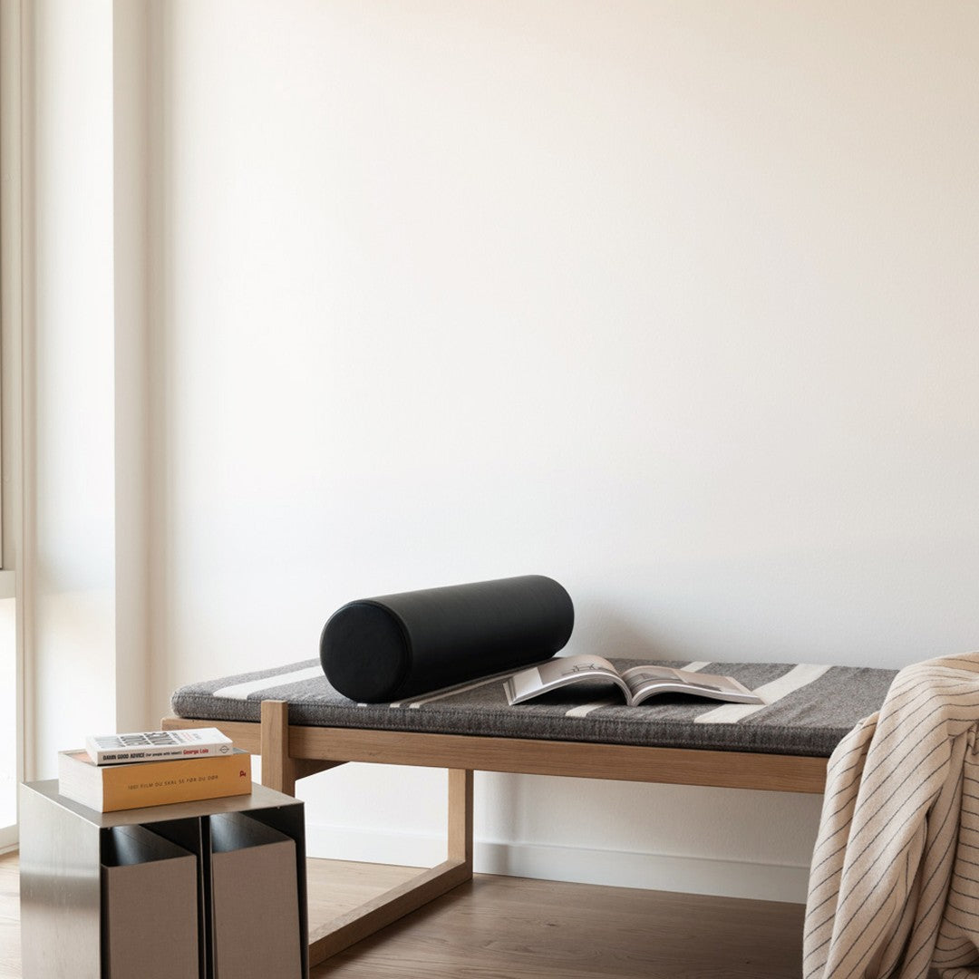 Black cylindrical pillow on a dark gray textured bedspread, paired with a light striped throw.
