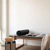 Black cylindrical pillow on a dark gray textured bedspread, paired with a light striped throw.