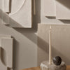 Neutral tones with soft beige textures and geometric patterns; features a slim white candle and dark round stone.