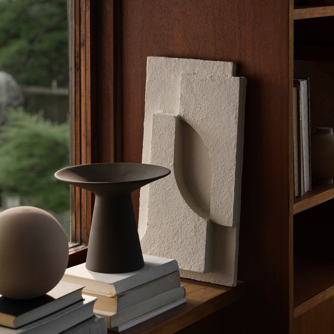 Neutral-toned textured wall art with organic shapes, complemented by a matte black vase and soft beige decor pieces.