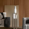 White vase on sleek silver stand, surrounded by black and white abstract art and warm wooden panels. Modern, minimalistic design.