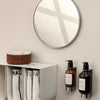 Round mirror reflecting light, black and amber bottles on a white shelf, and white towels with black lettering.