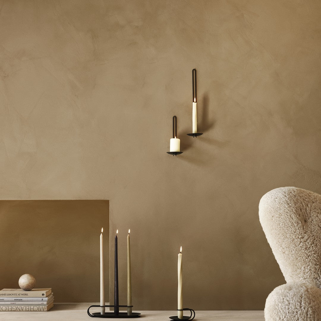 Minimalist wall with tan clay texture, featuring black and cream candle holders, and black and ivory taper candles.