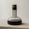 Elegant glass carafe with a sleek gray body, dark red wine, and a gold and black cap. Modern minimalist design.