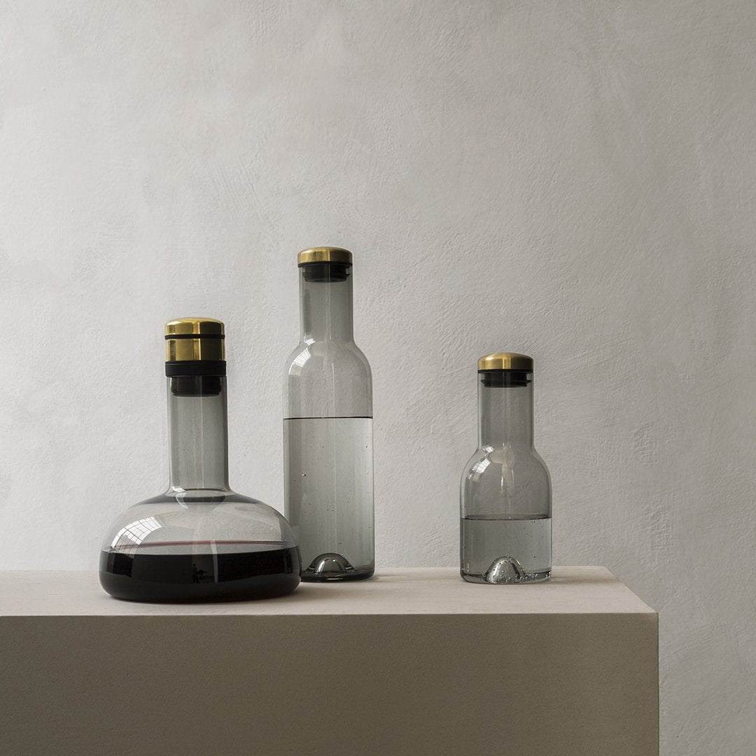 Elegant glass bottles in clear, frosted, and dark tones with gold accents, showcasing modern minimalist design.