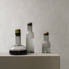 Elegant glass bottles in clear, frosted, and dark tones with gold accents, showcasing modern minimalist design.