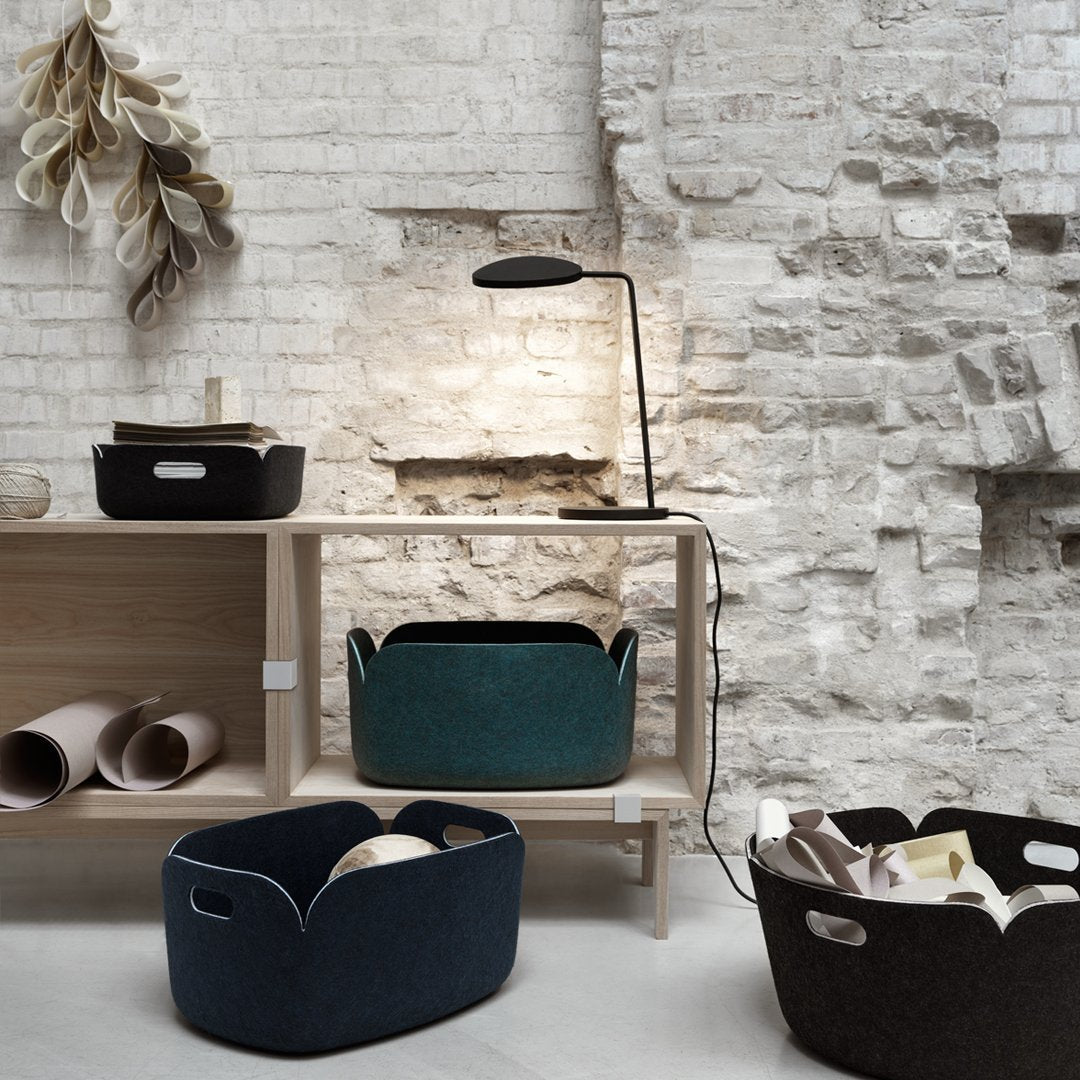 Black, dark teal, and navy felt storage baskets with curved edges against a textured white brick background.