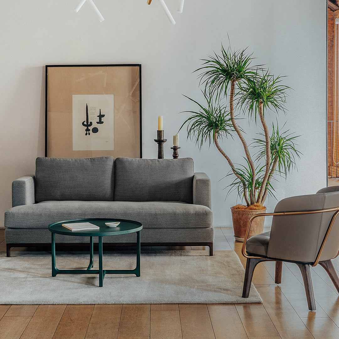 Modern gray sofa with a plush texture, paired with a green table, against a light wooden floor and neutral wall decor.
