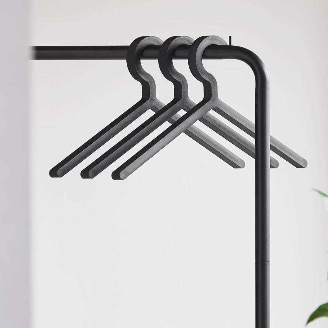 Four sleek black hangers on a minimalist black rack, set against a soft white background. Perfect for modern spaces.
