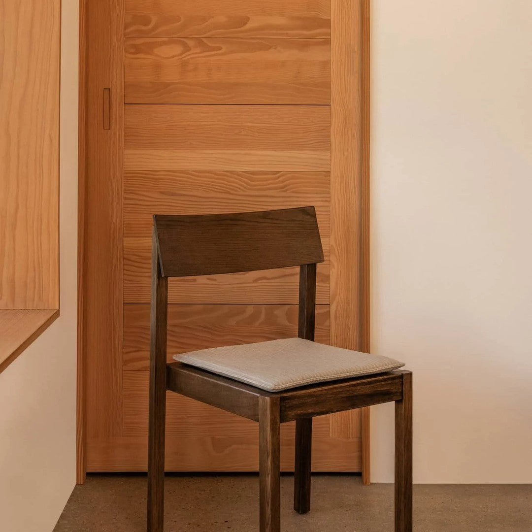 Dark wood chair with light gray cushion against a warm wooden background. Minimalist design with natural tones.