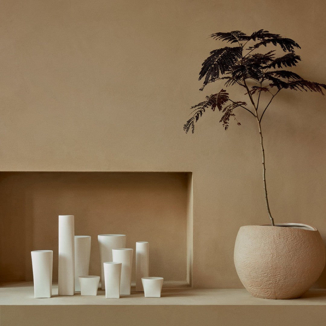 White ceramic vases in various shapes and sizes on a textured beige background. Simple, modern aesthetic.