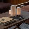 Soft white cylindrical lamps on a wooden table, complemented by black and beige books and a textured surface.