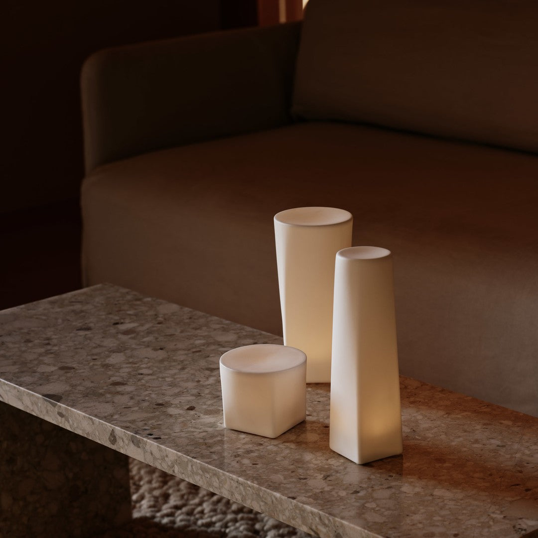 Set of three modern ivory candle holders with smooth, geometric shapes on a textured stone table.