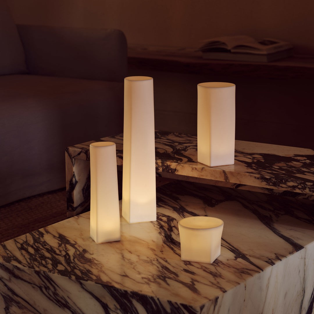 "Set of glowing white candleholders on a marble tabletop with rich brown and beige patterns."