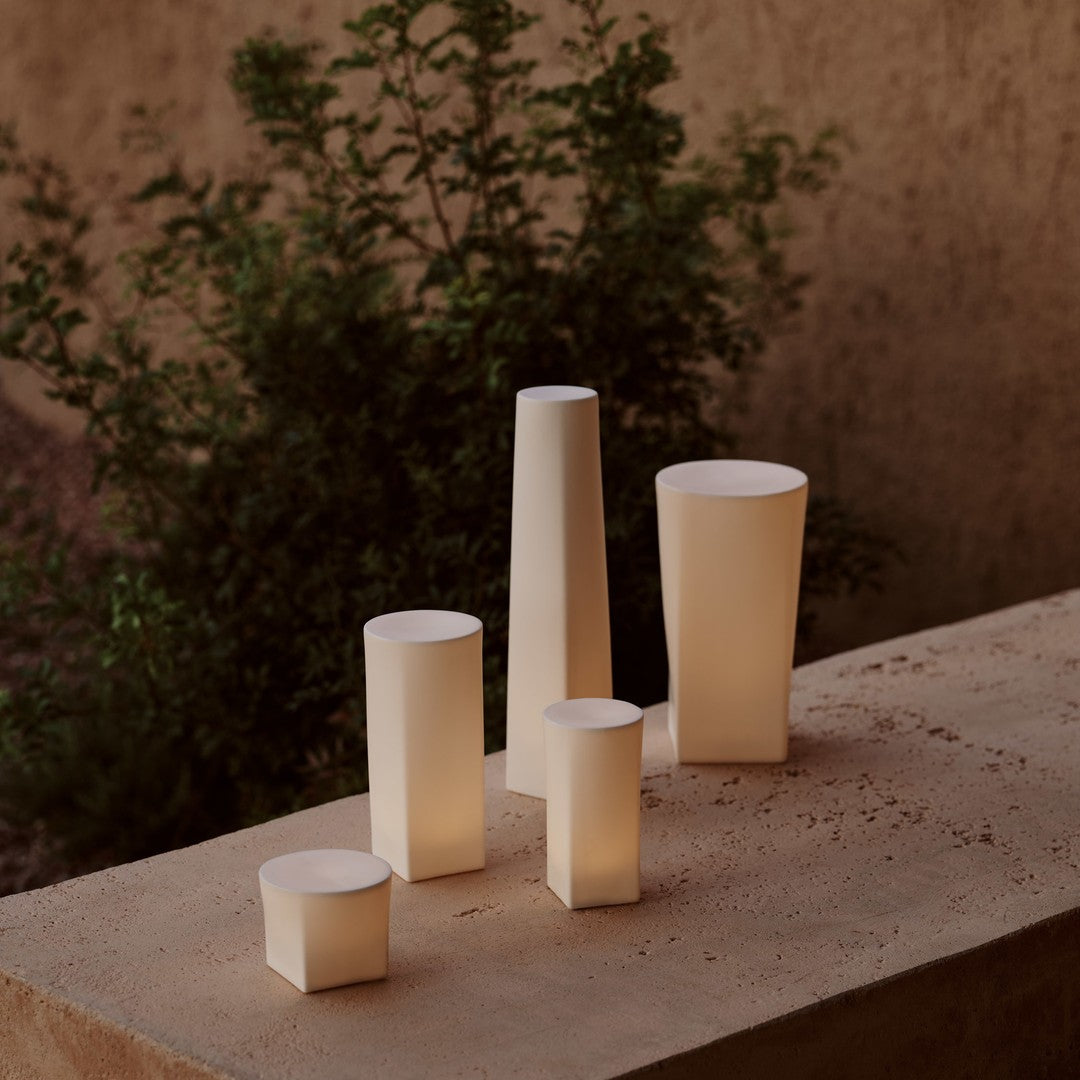 Set of five minimalistic white ceramic vases with soft, cylindrical shapes against a textured earthy background.