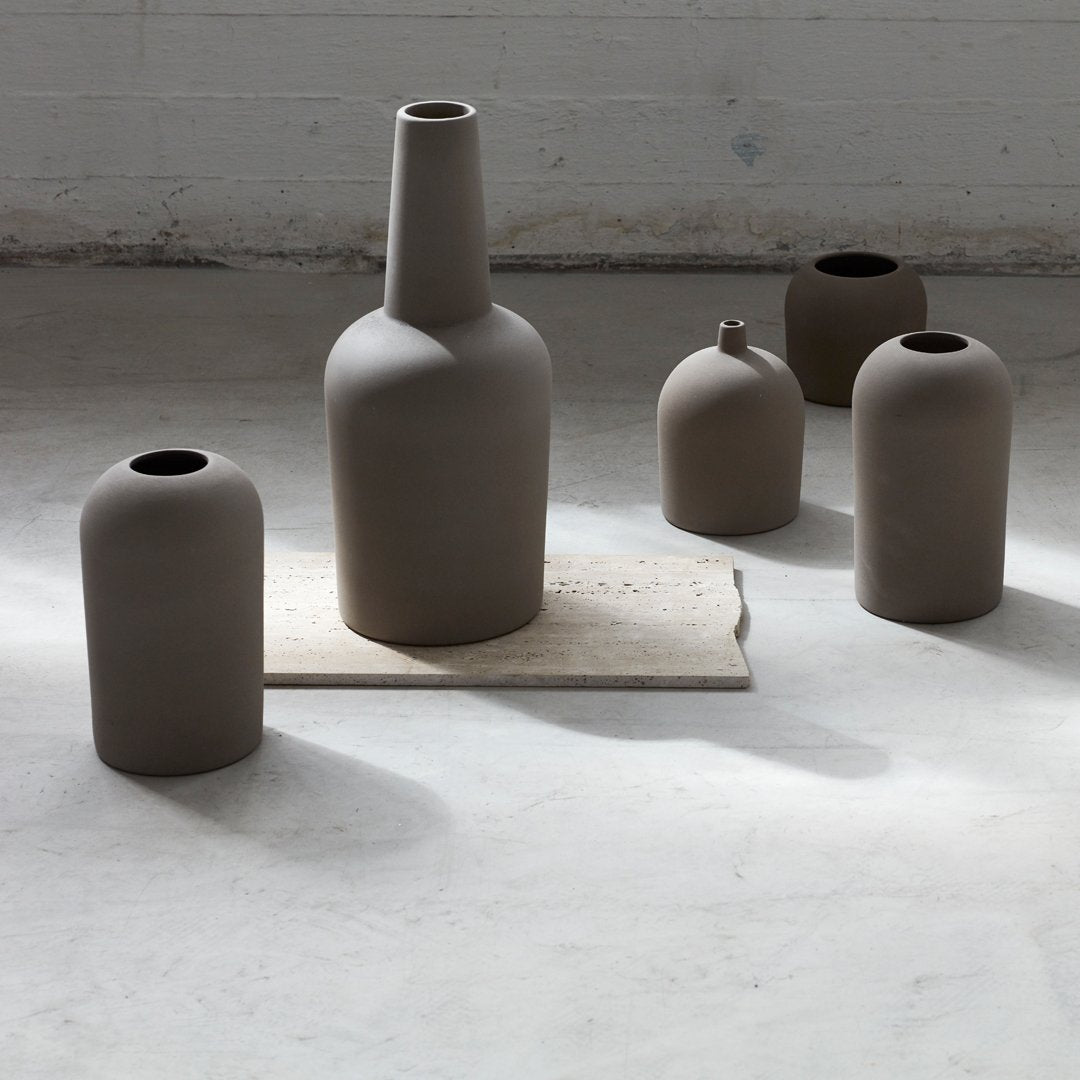 Set of five matte, neutral-toned ceramic vases in organic shapes with a subtle, textured finish on a light surface.