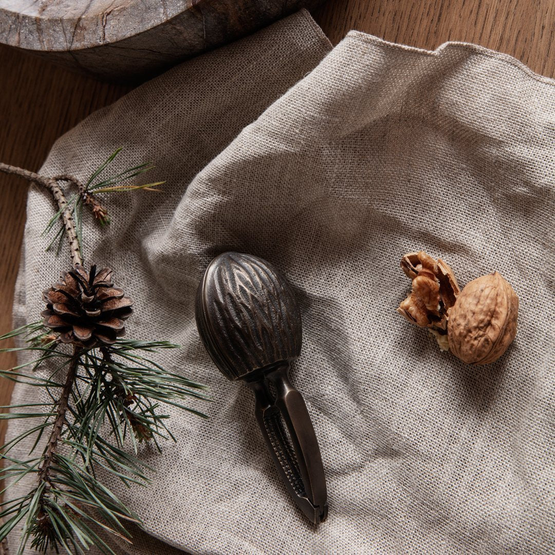 Rustic brown nutcracker on textured beige fabric with green pine needles and pinecone accents.