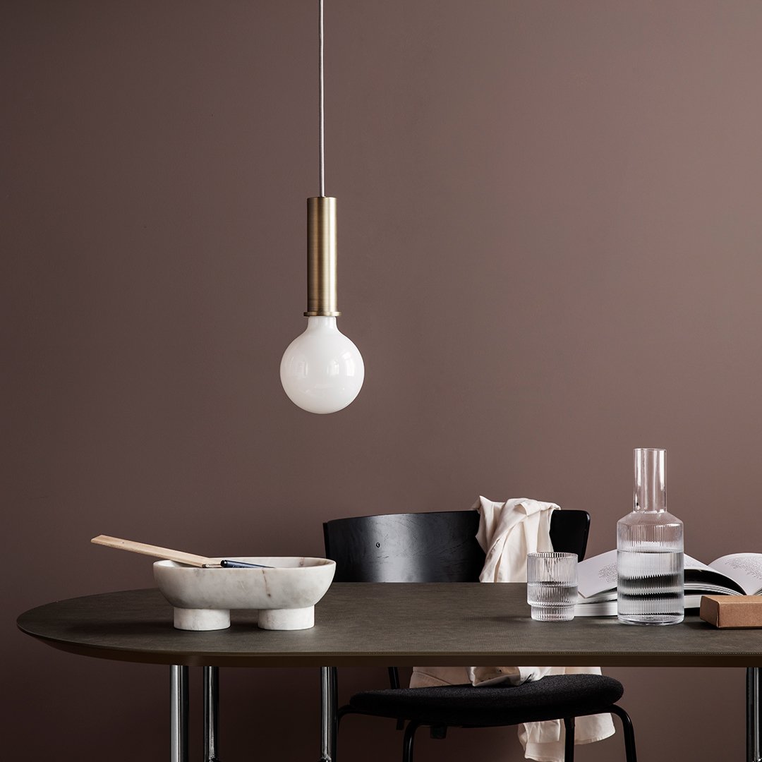 White globe pendant light with a brass accent hanging above a sleek, dark wooden table against a brown backdrop.