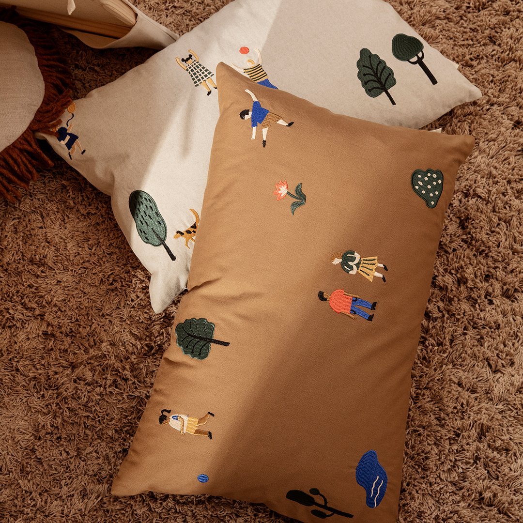 "Two decorative pillows in brown and cream, featuring playful nature-themed patterns and colorful illustrations."