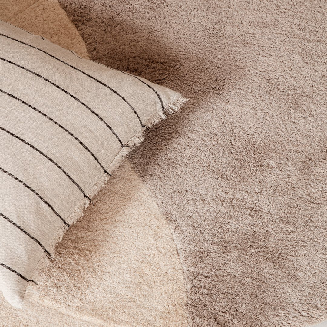 Beige and cream rug with a soft texture, featuring abstract shapes and a striped decorative pillow on top.
