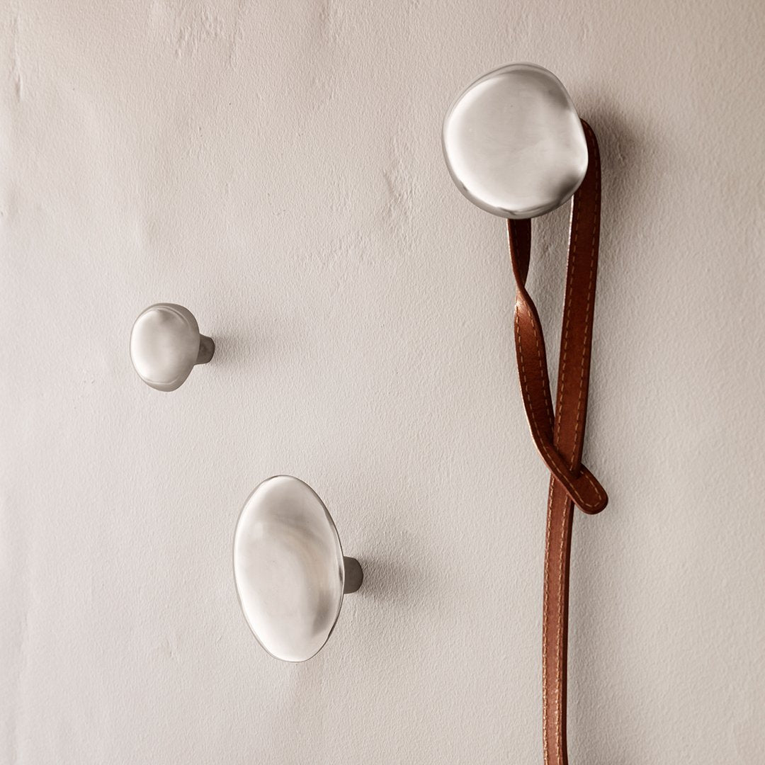 Set of three brushed metal hooks in varying sizes on a light textured wall, featuring a smooth, organic design.