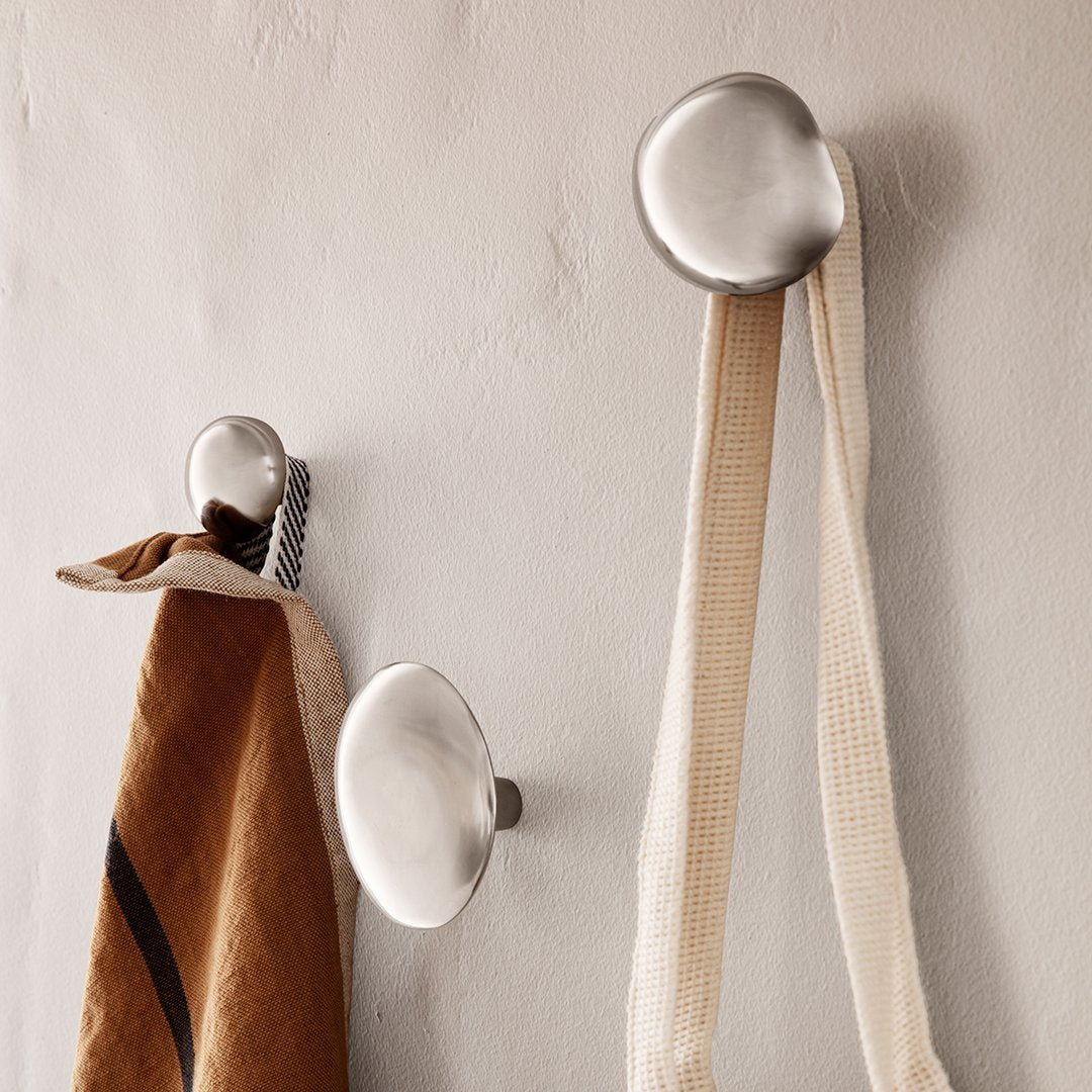 Sleek silver wall hooks against a neutral wall, showcasing smooth, rounded designs and earthy tones of the hanging items.