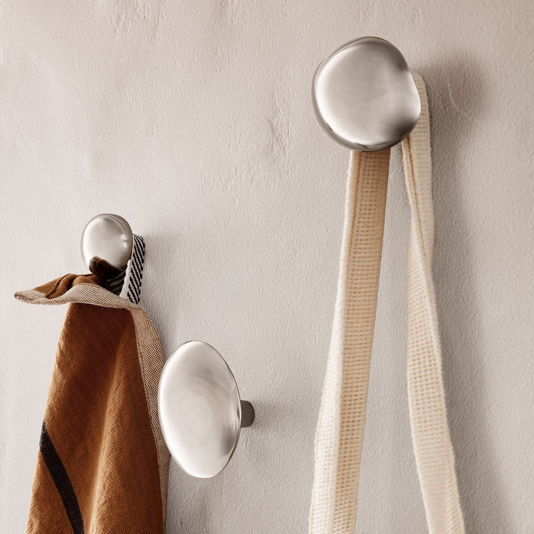 Sleek silver wall hooks with contrasting brown and cream fabric hanging, showcasing minimalist design and modern aesthetics.