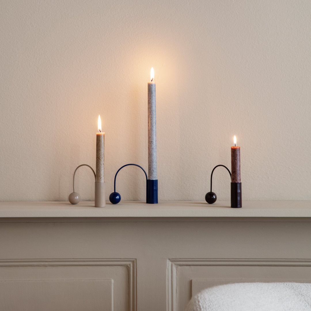 Modern candle holders in gray, navy, and copper hues, featuring sleek curved designs and glowing candles.