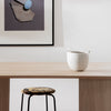 White textured basket on a wooden table, featuring a patterned stool with earthy tones and black legs. Minimalist decor.