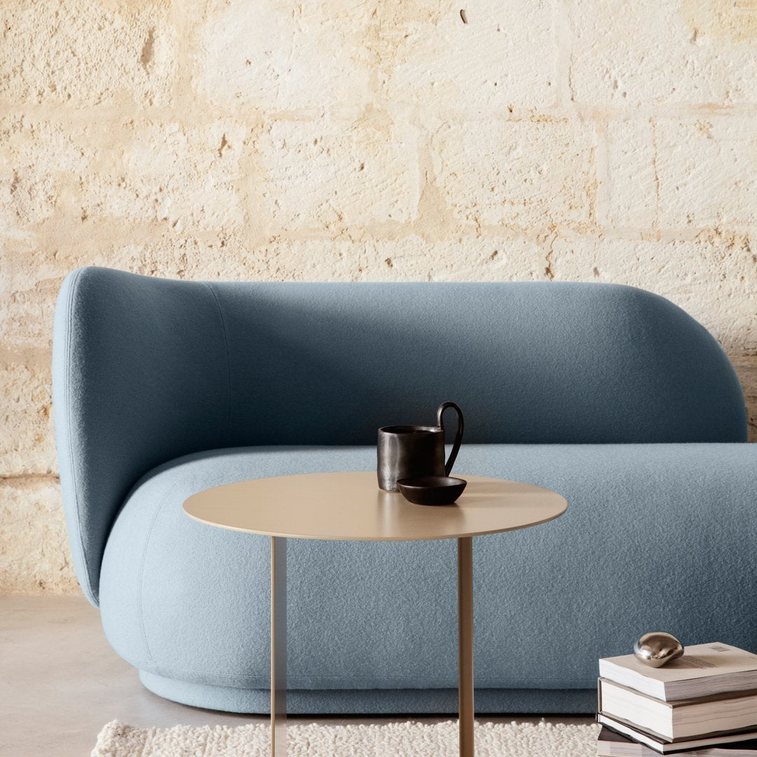 Soft blue curved sofa with a smooth fabric texture, complemented by a round gold coffee table against a neutral background.