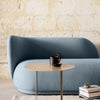 Soft blue curved sofa with a smooth fabric texture, complemented by a round gold coffee table against a neutral background.