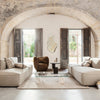 Modern living room featuring neutral beige sofas, a brown accent chair, and natural light from open wooden windows.