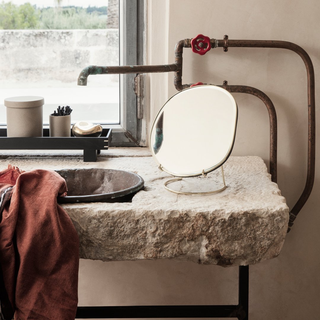 Elegant oval mirror with a gold finish against a rustic stone sink, complemented by earthy brown and white accents.