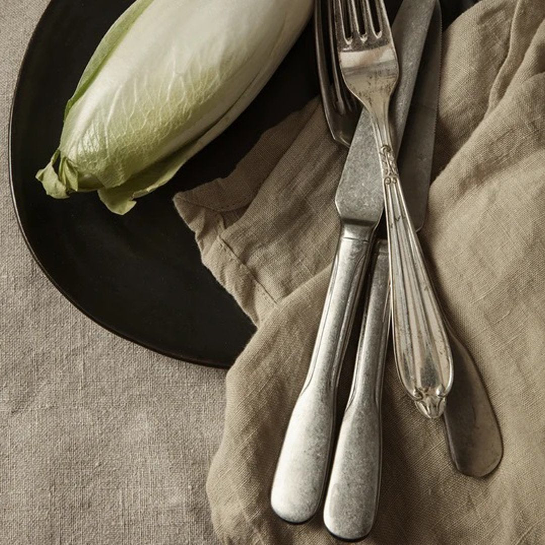 "Neutral tones with a green accent from the lettuce, paired with vintage silver utensils on a textured linen backdrop."