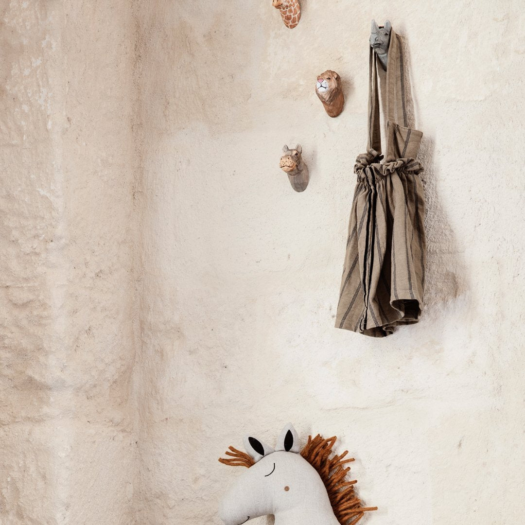 "Beige wall with textured stone, striped brown and cream hanging bag, and a soft white and brown unicorn plush toy."