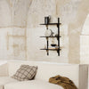 Black metal shelf against a textured beige wall, with neutral-colored decor and a checkered cushion in soft tones.