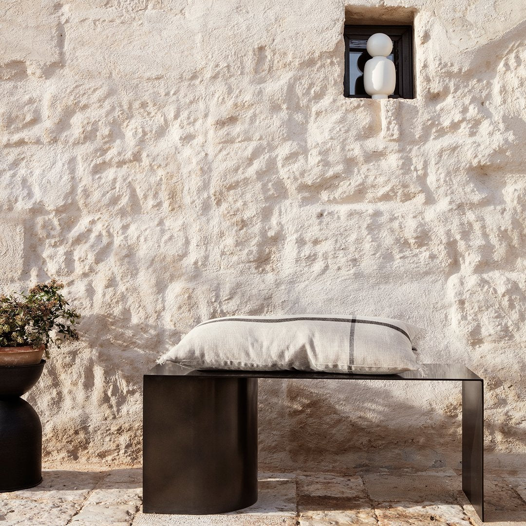 Minimalist black bench with a light beige cushion, set against a textured stone wall; modern and elegant design.