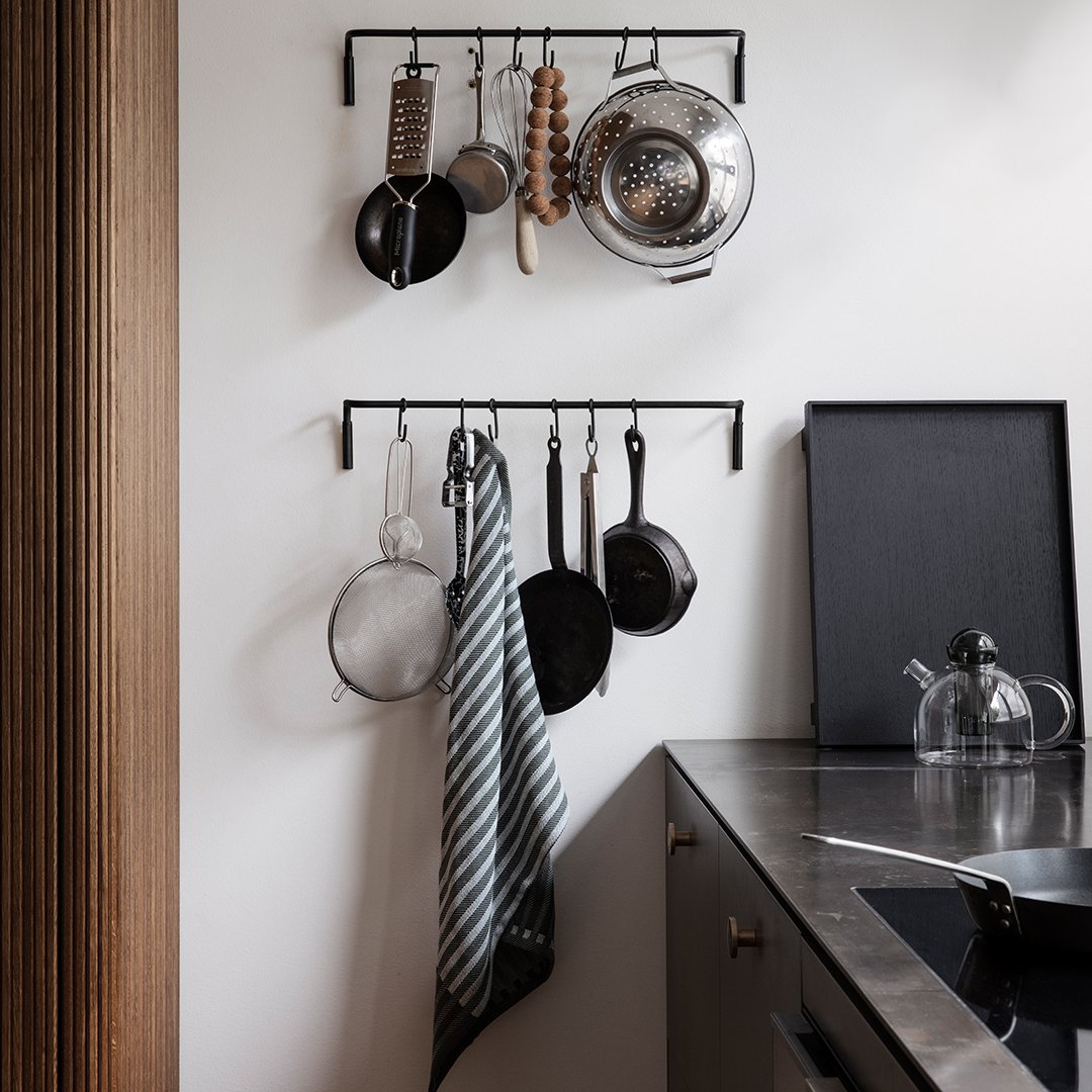Black metal hanging rack with silver pots and a striped gray and white towel in a modern kitchen setting.