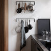 Black metal hanging rack with silver pots and a striped gray and white towel in a modern kitchen setting.