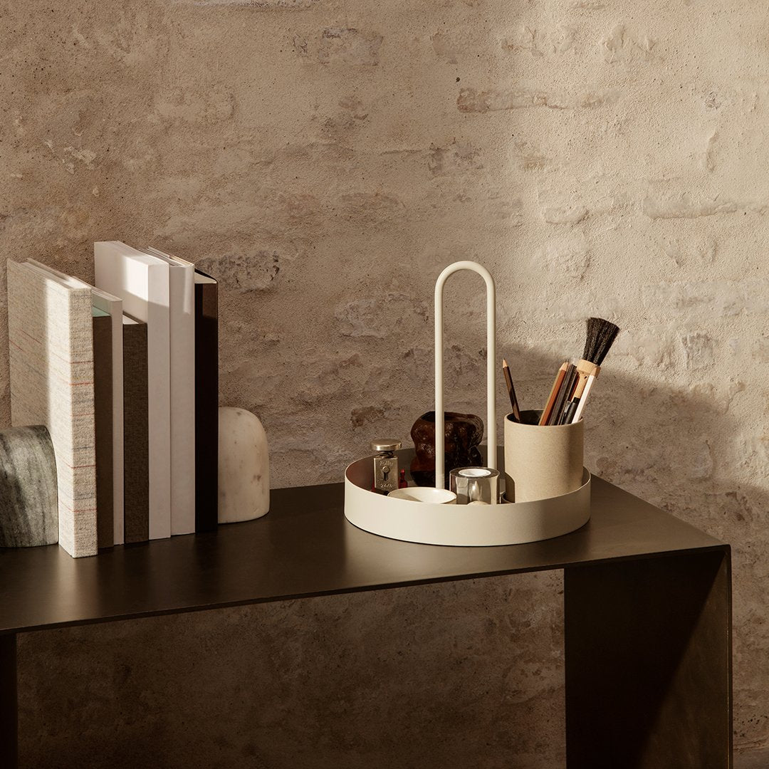 Cream circular organizer with minimalist design, set against a textured stone wall and dark wooden table.