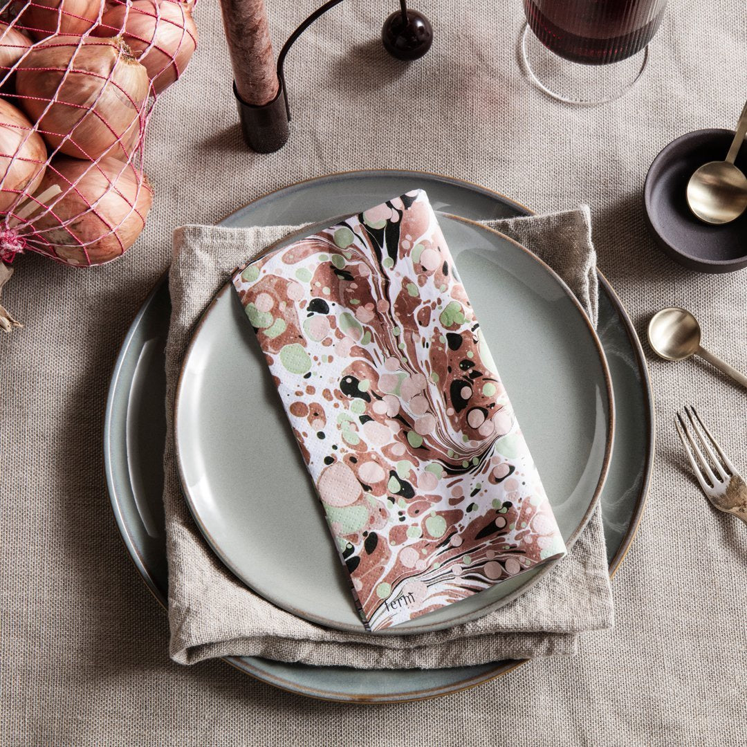 "Marble-patterned napkin in soft pink, green, and black on textured linen with pastel plates."